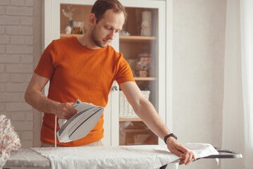 Young man ironing children's sheet on ironing board at home