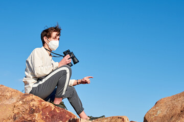 A front view of an explorer from Spain wearing a mask sitting on a rock looking into the camera