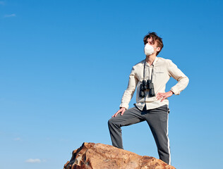 A shallow focus of a confident young man from Spain standing on a cliff wearing a face mask and a...
