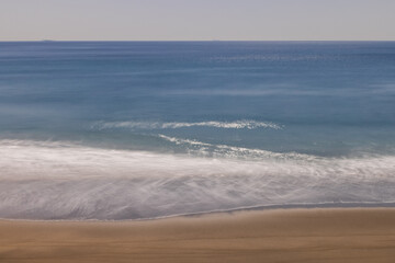 海岸に打ち寄せる波が作る抽象、波に反射する太陽の光、水平線を航行する船、長秒露光