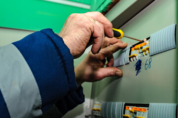 An electrician checks the electricity in the switchboard with a screwdriver