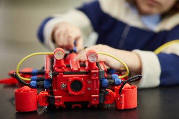 Close up of unrecognizable boy boy building red robotic machine while enjoying engineering class in development school , copy space