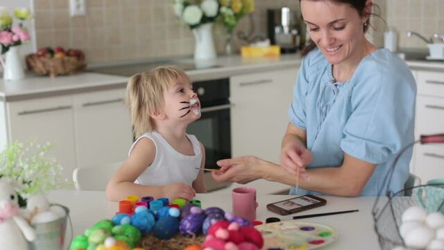 Mother painting on little blond toddler boys' face easter bunny at home