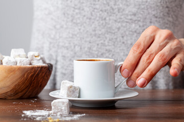 A caucasian Turkish woman is drinking traditional Turkish coffee from special cup. The coffee is served with Turkish delight  on the side of the plate. Close up concept image.