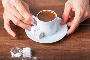 A caucasian Turkish woman is drinking traditional Turkish coffee from special cup. The coffee is served with Turkish delight  on the side of the plate. Close up concept image.
