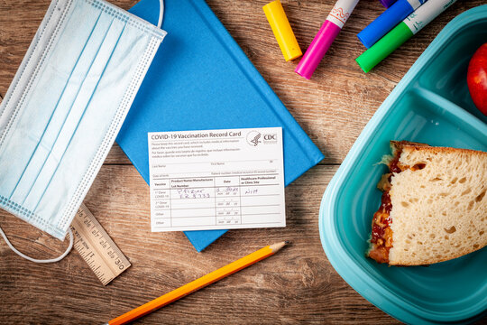 04-02-2021 Clarksburg, MD, USA: It is expected that kids will be getting vaccines before the start of the school year. Concept image showing a vaccination record card on an elementary school desk