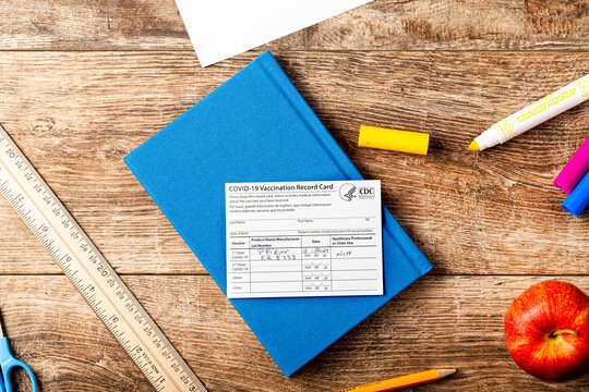 04-02-2021 Clarksburg, MD, USA: It is expected that kids will be getting vaccines before the start of the school year. Concept image showing a vaccination record card on a school desk.