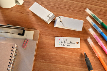 There is a a word card with chief information officer written on it. They are on the desk along with stationery such as notebooks and colored pens.