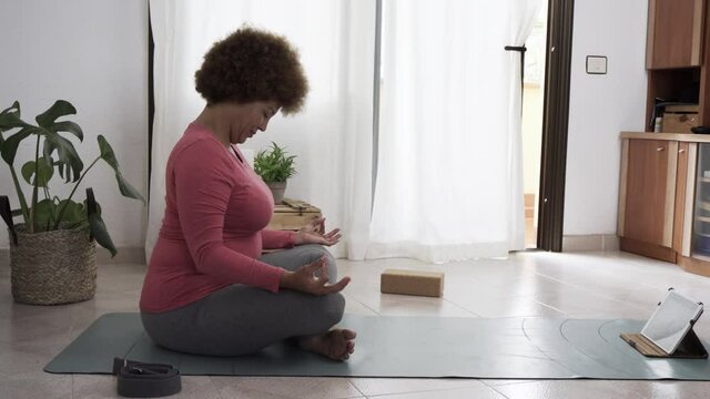 African senior woman exercising while doing online yoga class at home - Sport and healthy lifestyle concept