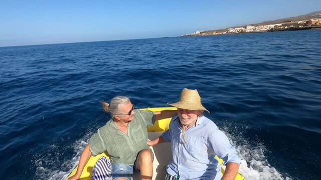 Beautiful and cute couple of seniors or old people in the middle of the sea driving and discovering new places with small boat. Mature woman holding a phone and taking a selfie with hew husband
