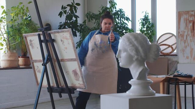 A woman paint artist drawing on a canvas taking a greek head sculpture as a reference