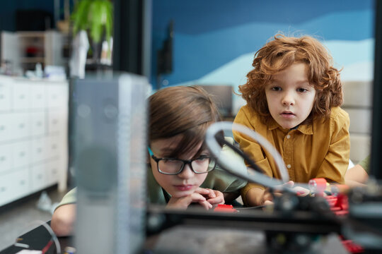 Portrait of two schoolboys watching 3D printer during engineering class at modern school, copy space