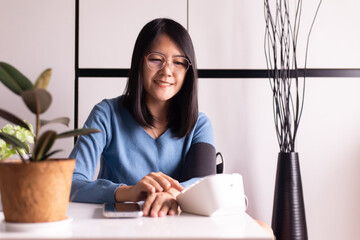 Happy asian woman using blood pressure & heart rate monitors in yourself at home