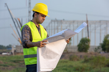 construction worker hard hat supervising a project, standing with blueprints on the construction site.