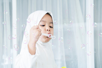 Cute Muslim little girl blowing soap bubbles at home