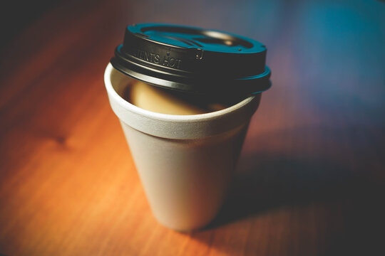 Styrofoam coffee cup with plastic spoon and used creamer container in  foreground and human elbows on table in background. Stock Photo