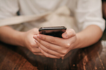 Close-up image of male hands using smartphone searching or social networks concept, hipster man typing an sms message to his friends on vintage wood table in cafe