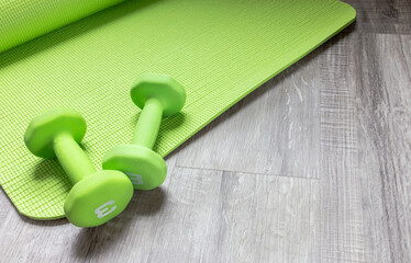 Set of indoor workout equipment, green dumbbells and mat flat lay on wood floor. Personal training by yoga and lifting weight for health and wellness, exercise lifestyle at home. Top view object.