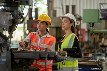 Two technician engineer working and inspecting metal component at lathes machine in industry factory.
