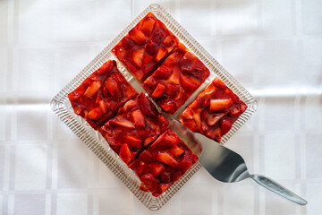 Strawberry cake with a server on a white table. Homemade sweet pastry portion sliced into delicious pieces. Red fruit pie ready to eat.