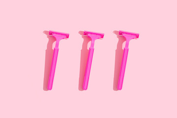Minimal concept: three raspberry-colored ladies' razors with hard shades on a pink background. Feminine bodycare.