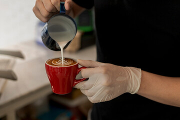 Close up barista pouring steamed milk into coffee cup making beautiful latte, cappuccino art Rosetta pattern. Close up barista hands pouring warm milk in red coffee cup for making latte art.