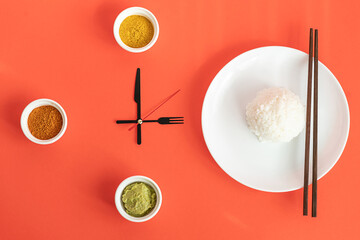 Time for eating dinner. Concept of lunchtime, diet and weight loss. Fork and knife as the clock hands. Asian food, rice with spices