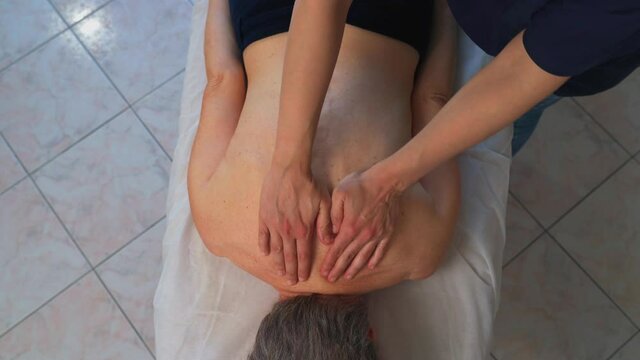 Some panning shots, zenithal, near a back massage to a Caucasian woman, given by a physiotherapist in a health clinic.