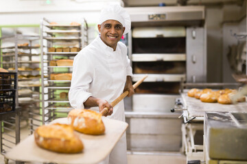 Male baker pulls hot bread out of the oven at the bakery