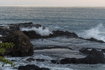 Beautiful view of the ocean waves chasing in rocks with a magical sunset in the horizon