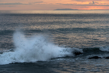 Beautiful view of the ocean waves chasing in rocks with a magical sunset in the horizon