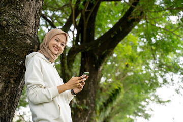 smiling beautiful young muslim woman using mobile phone during exercise break outdoor