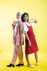 Obraz premium Closeup portrait of two young beautiful asian woman isolated on yellow background.