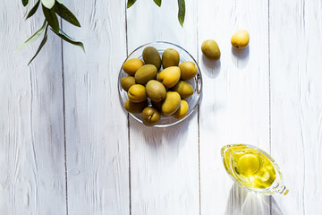 Olive oil and bowl of green olives on a white wooden table. Modern minimal still life, glass bowl...