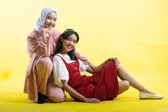 Closeup portrait of two young beautiful  asian woman isolated on yellow background.