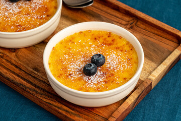 Creme brulee in ramekin on wooden tray on dark linen tablecloth. Close up french vanilla cream dessert. Burned cream. Spanish crema catalana with caramelized sugar.