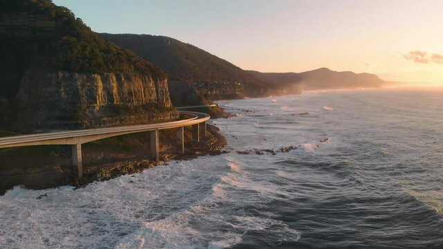 Vehicle Drives Along Sea Cliff Bridge Sunrise Aerial Track Forwards - Sunrise Australia Ocean