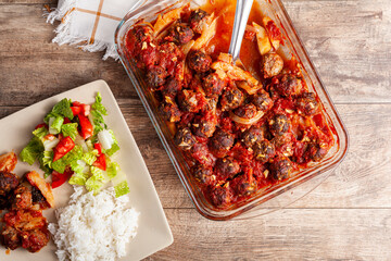 Traditional Turkish recipe, meatballs in tomato sauce, potatoes and onion rings cooked in oven. The meal called kofteli patates is served with salad and Turkish rice pilav