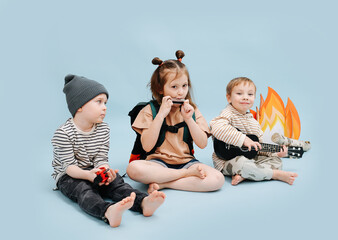 Slightly bored children sitting next to fake campfire, playing their instruments