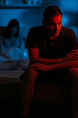 Couple issue. Domestic violence. Abuse harassment. Aggressive man sitting on bed with scared...
