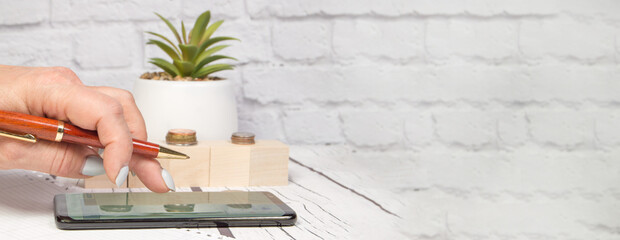 Female accountant uses a mobile phone with a pen to calculate profit and loss, business concept, office background, banner