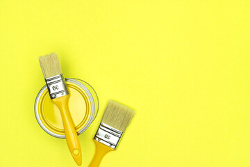 two yellow paintbrushes and can of yellow paint on bright yellow background. top view, flat lay.