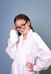 pretty young girl with black glasses and white work lab coat iis posing in front of blue background