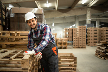 Portrait of warehouse worker leaning on wooden palette in factory storage room.