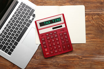 Modern calculator with text TAX TIME and laptop with notebook on wooden background