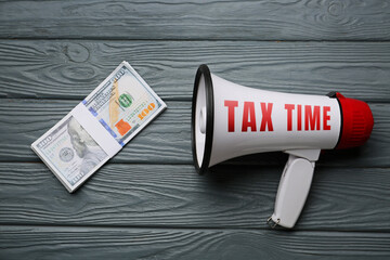 Megaphone with money on grey wooden background. Concept of taxes