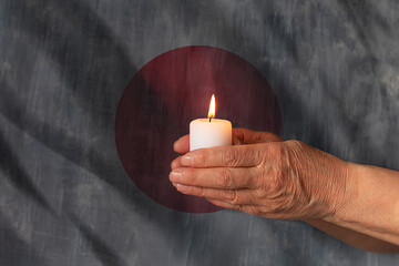 Hands hold a candle against the background of the flag of Japan. The concept of mourning and sadness in the country, terrorism.