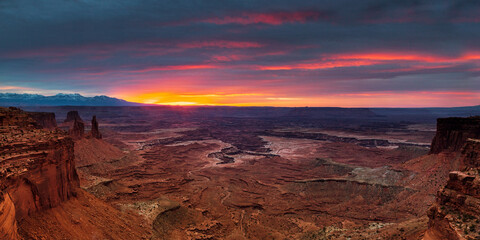 Panoramic  view above Mesa Arch towards Washer Woman Arch and the La Sal Mountains under a fiery sunrise