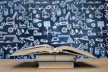 Blackboard with hand-drawn math-related icons. Books stacked on the desk. Education concept.