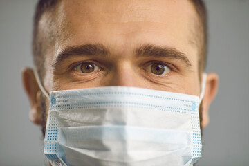 Closeup studio portrait of caucasian man in face medical mask with wide-open surprised eyes. Male face with shock emotion from coronovirus covid 19 pandemic consequences lockdown prolongation